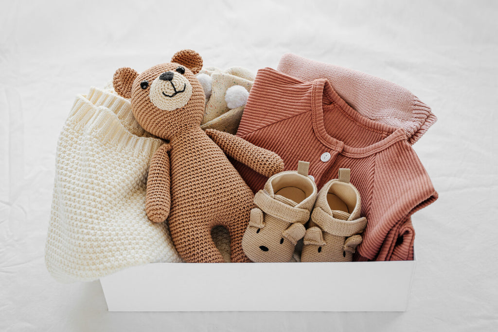 Curated gift box featuring high-end baby knitwear, soft pink outfit, and handmade teddy bear from Bambino Babe